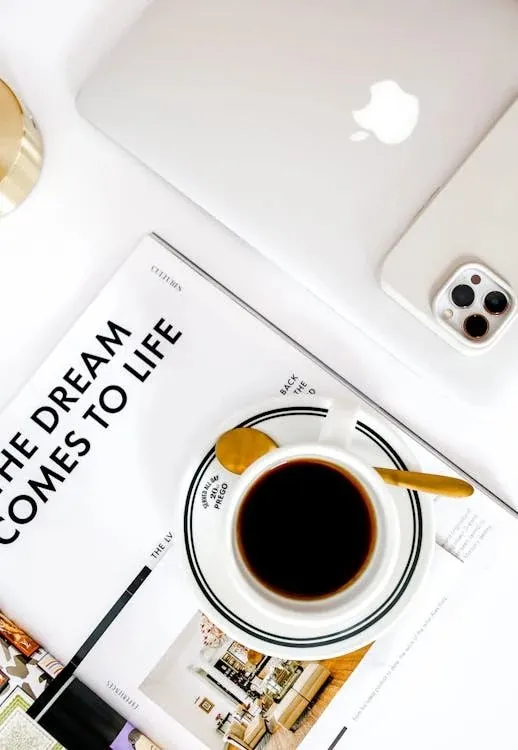 A cup of black coffee on a saucer next to an open magazine