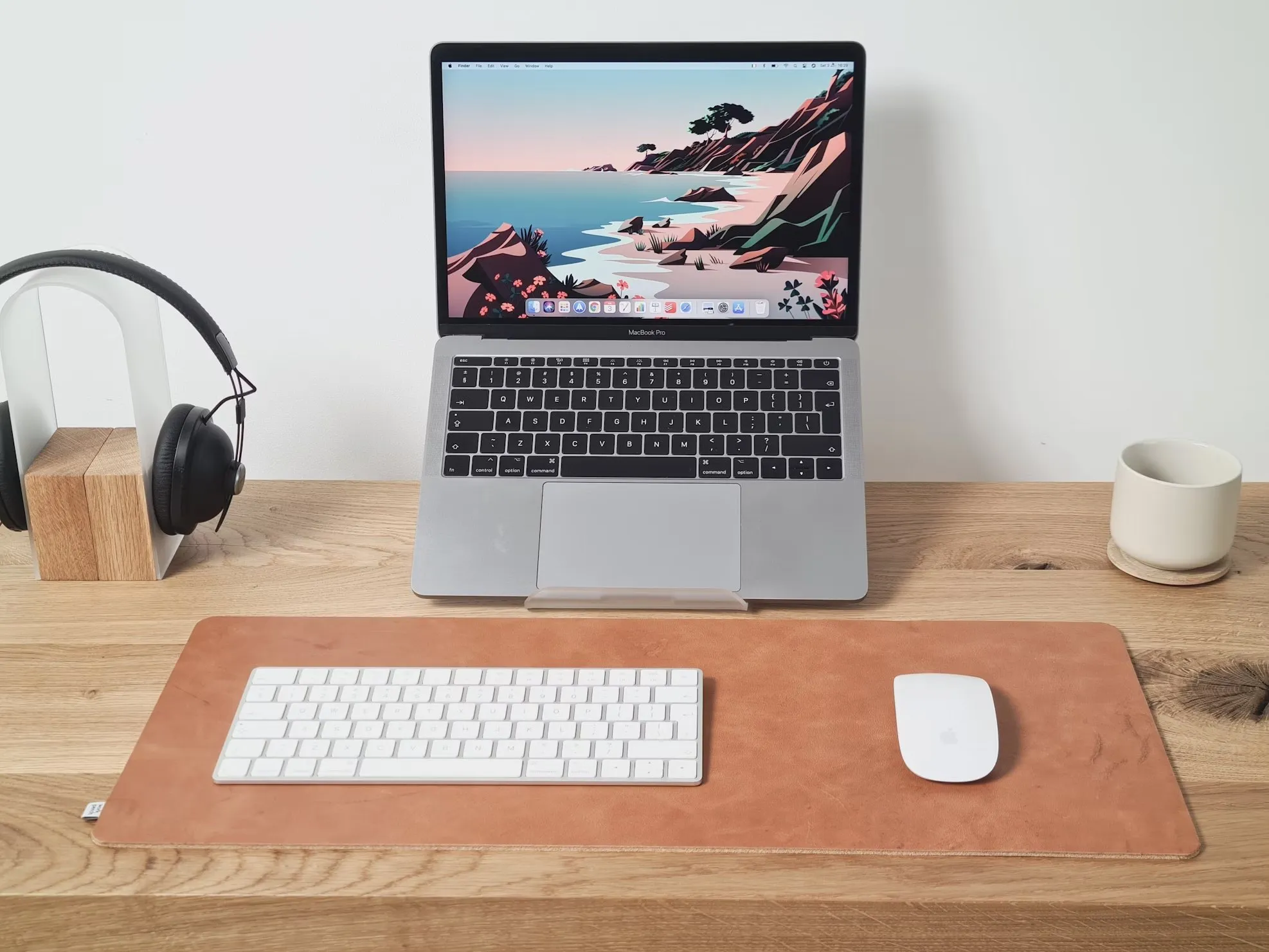 A laptop on a stand with a keyboard, mouse and headphones on a wooden desk
