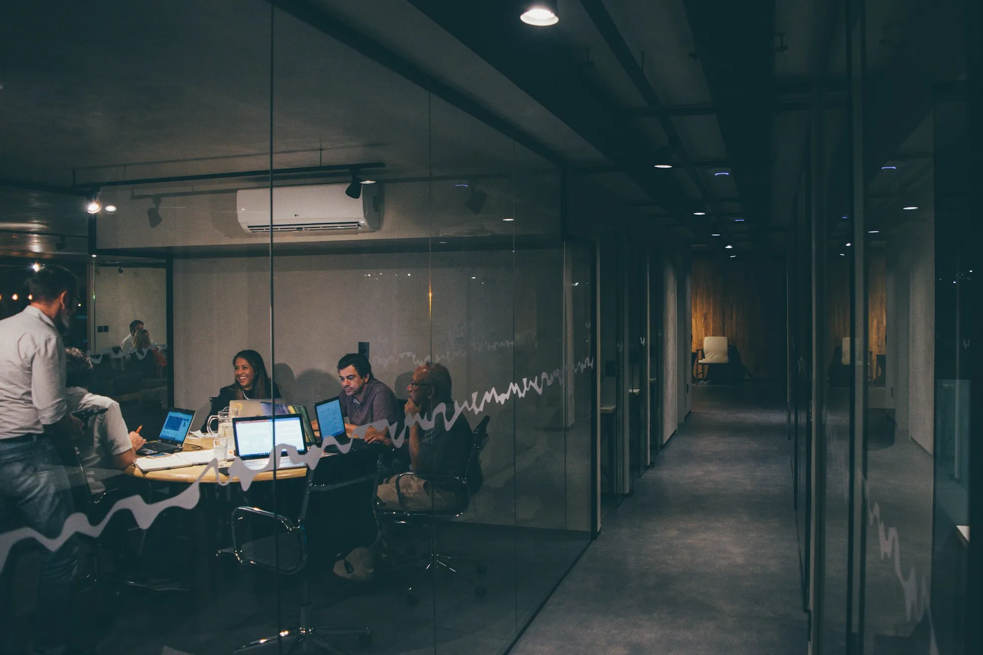 A team talking around a meeting table with laptops in an office at night