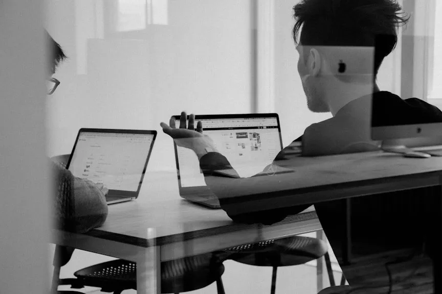 Black and white photo of people working on laptops at a long office table