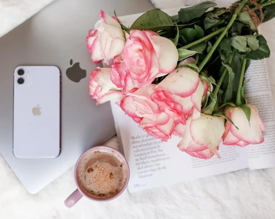 Pink roses, a smartphone, a laptop and a cup of coffee on a white table