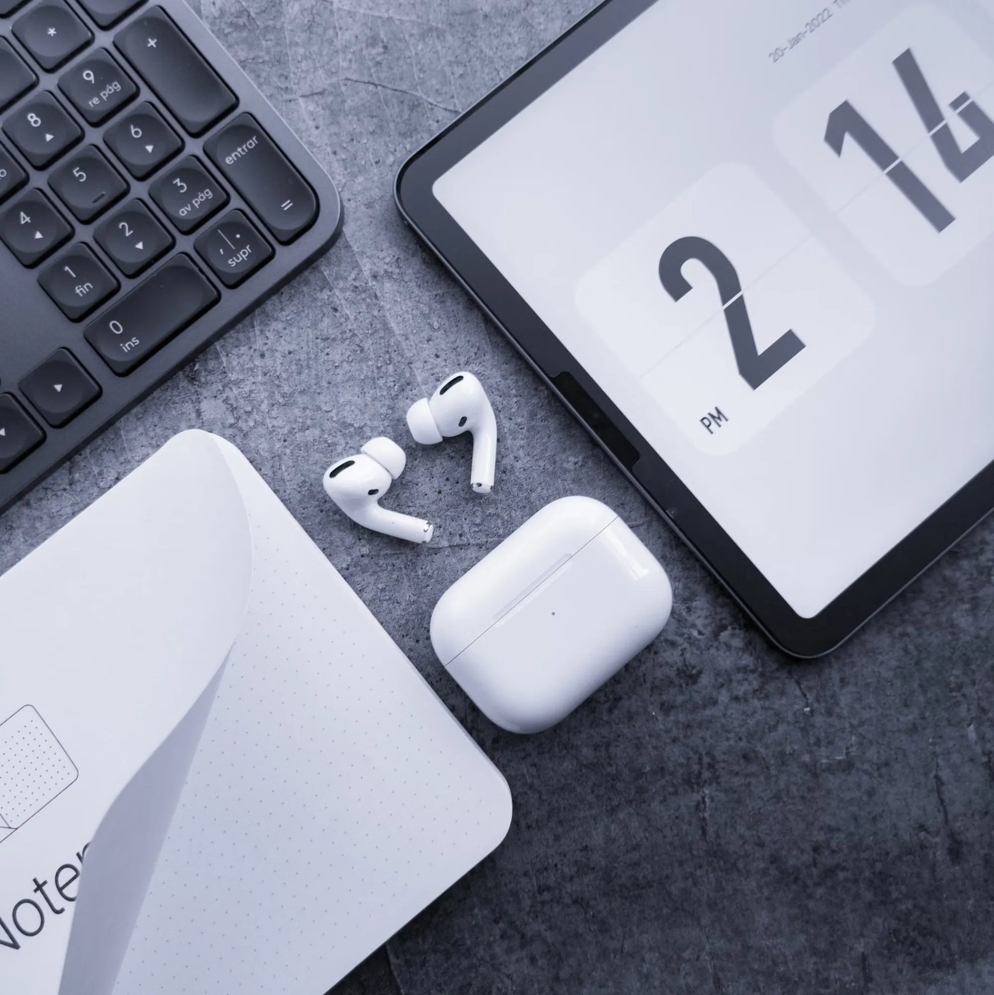 A tablet, keyboard, wireless earbuds and a calendar on a grey desk