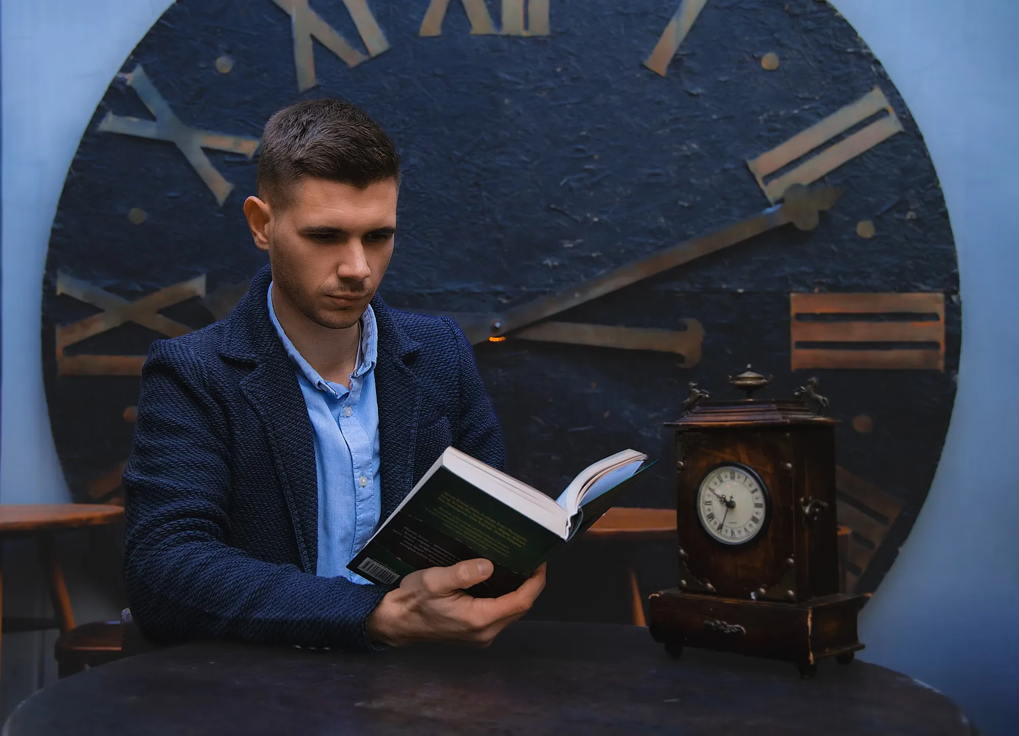 A man in a suit reading a book in front of a large clock