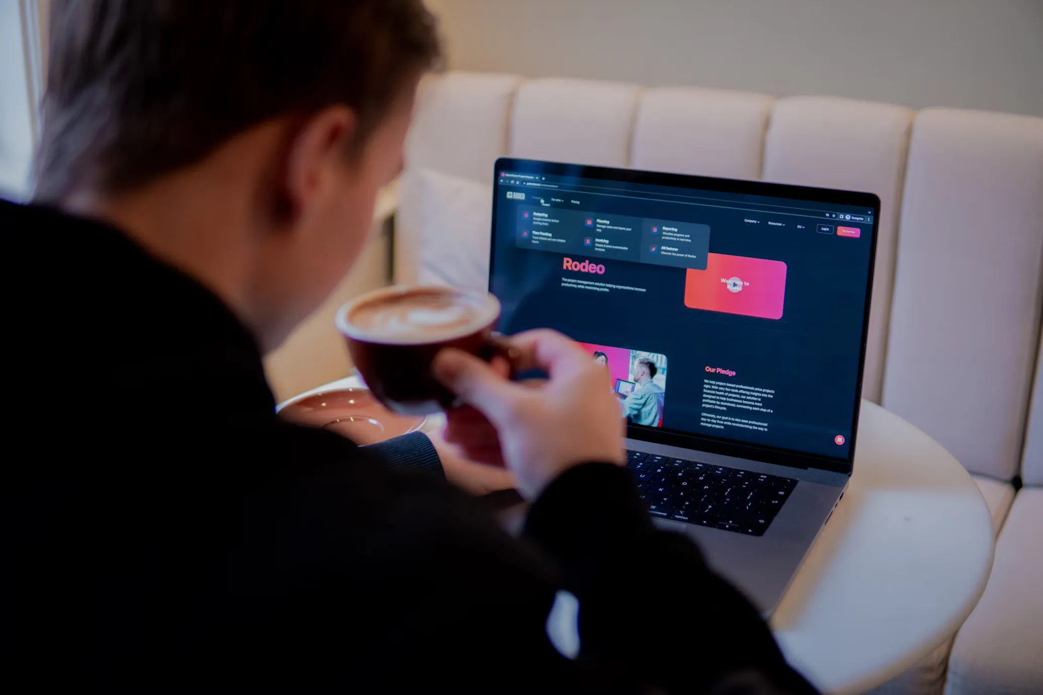 A man with a coffee cup looking at a laptop on a sofa